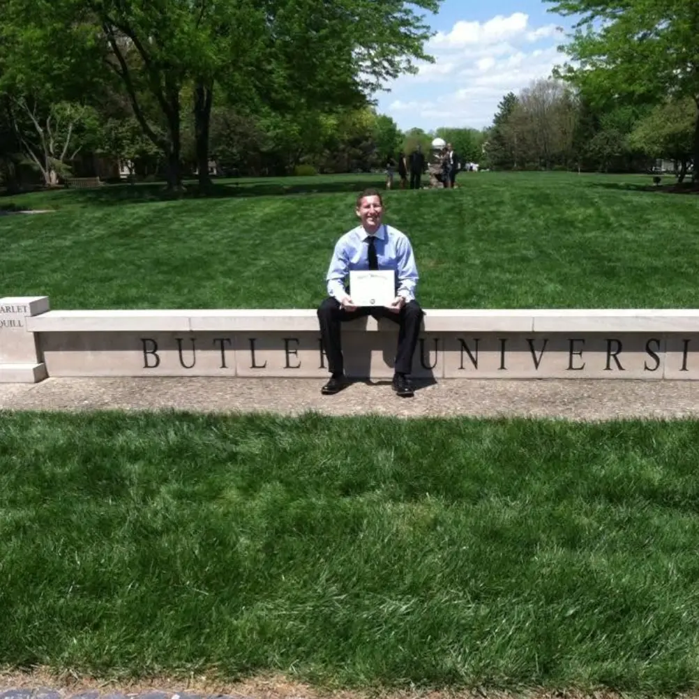 Michael Becker holding his diploma at the Butler University campus sign