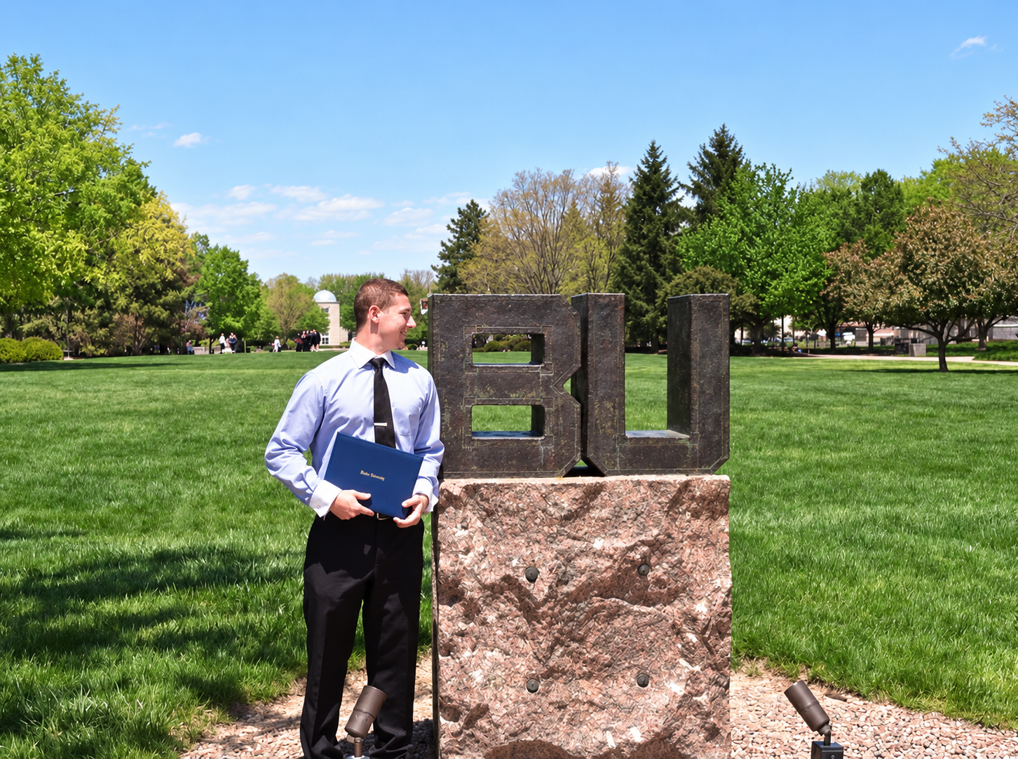 Michael Becker holding his diploma at the Butler University campus sign